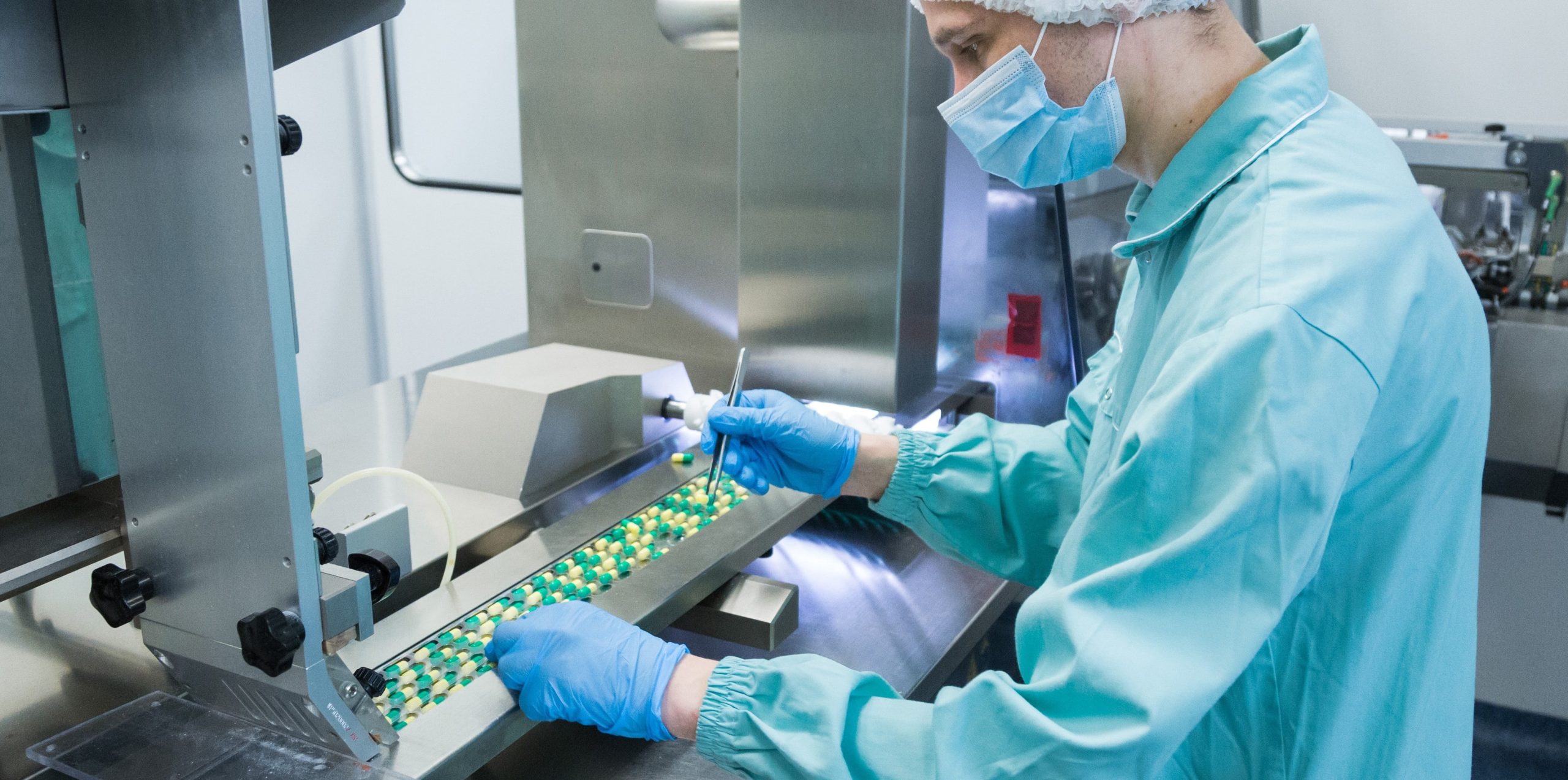 Pharmaceutical staff monitors capsule quality on an automated production line, representing OEM manufacturer Singapore services in healthcare product registration.