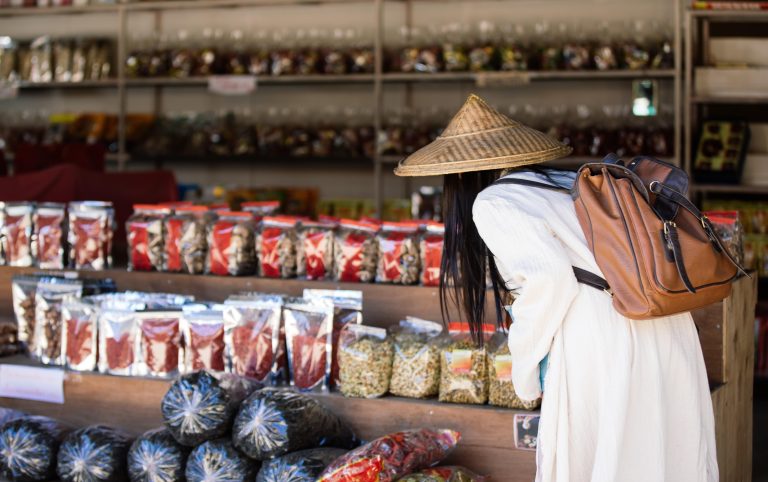 A woman browses traditional herbal supplements and dried health products, highlighting the diversity of Singapore supplements and their potential for halal certification and OTC manufacturing.